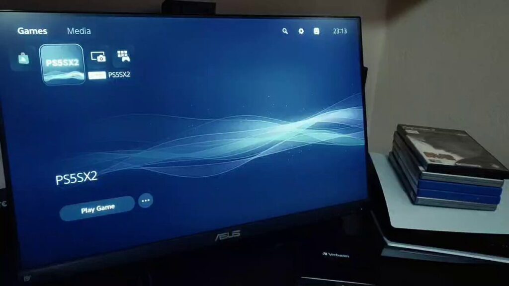PS5SX2 sulla schermata iniziale di una PS5 modificata accanto a una pila di giochi su disco